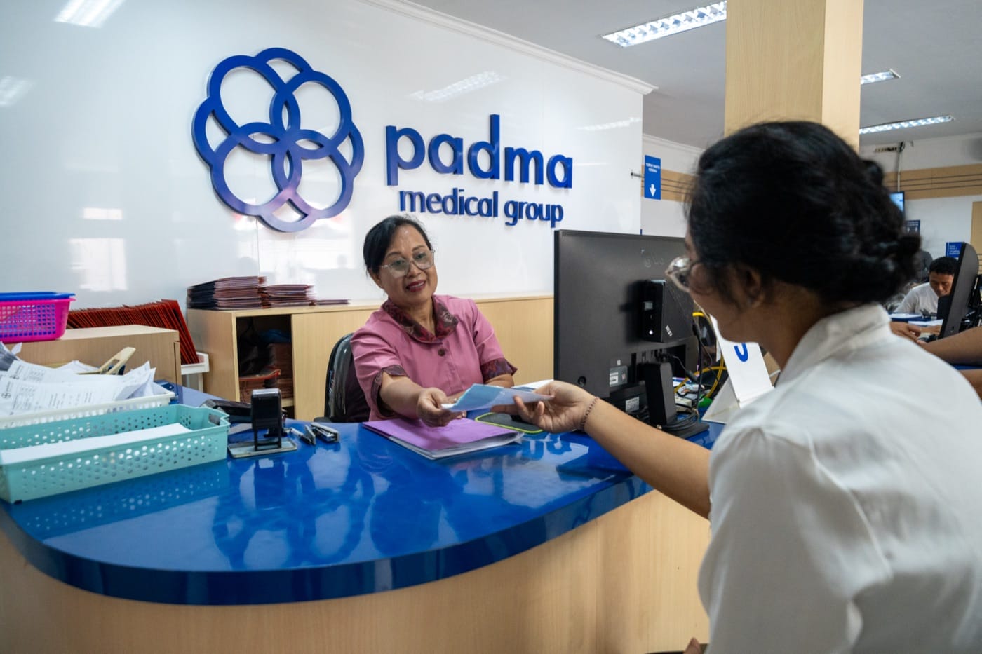 A Padma Care advisor handing a card to a member across the reception desk.